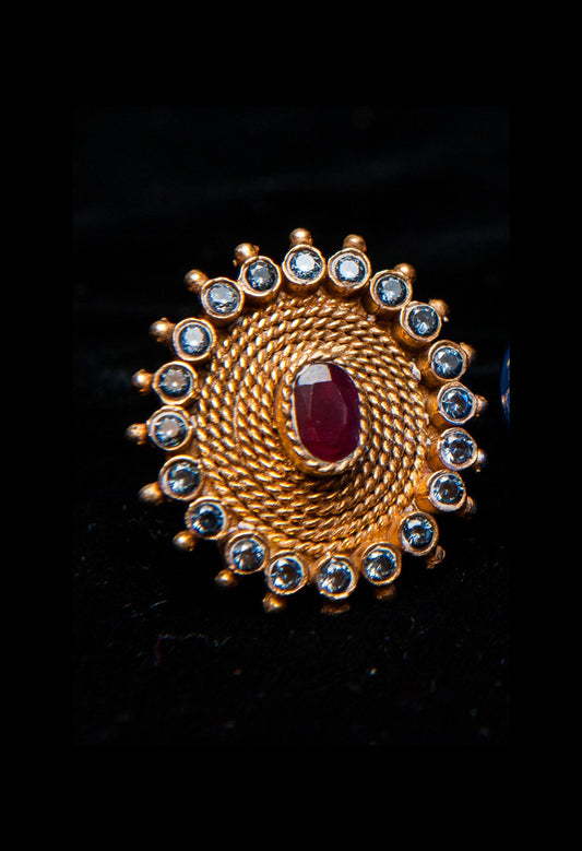 Gold ring with a red gemstone and smaller clear stones on a black background