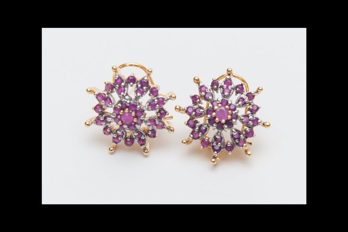 Pair of gold earrings with purple gemstones on a white background