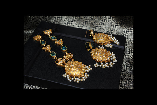 Gold and pearl jewelry set on a black box with a patterned fabric background