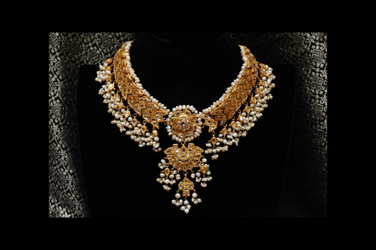 Ornate gold and pearl necklace on a textured black background
