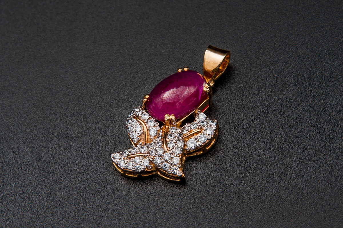Jewelry pendant with a red gemstone and diamond accents on a dark background