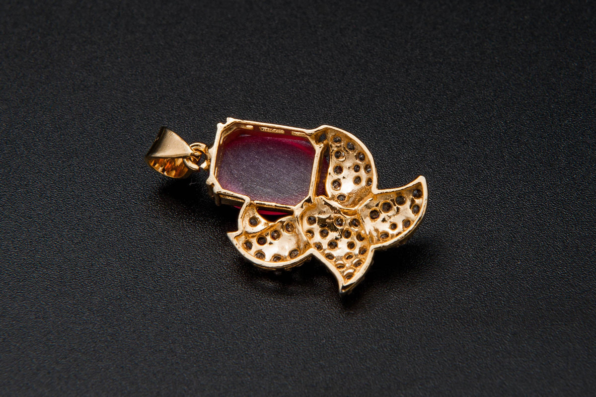 Gold pendant with a red gemstone on a black background
