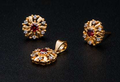 Gold jewelry set with floral designs and red gemstones on a black background