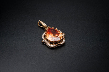 Gold pendant with a large orange gemstone on a black background
