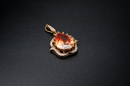 Gold pendant with a large orange gemstone on a black background