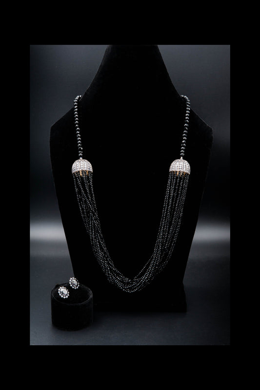 Elegant beaded necklace and earrings on a black stand against a dark background