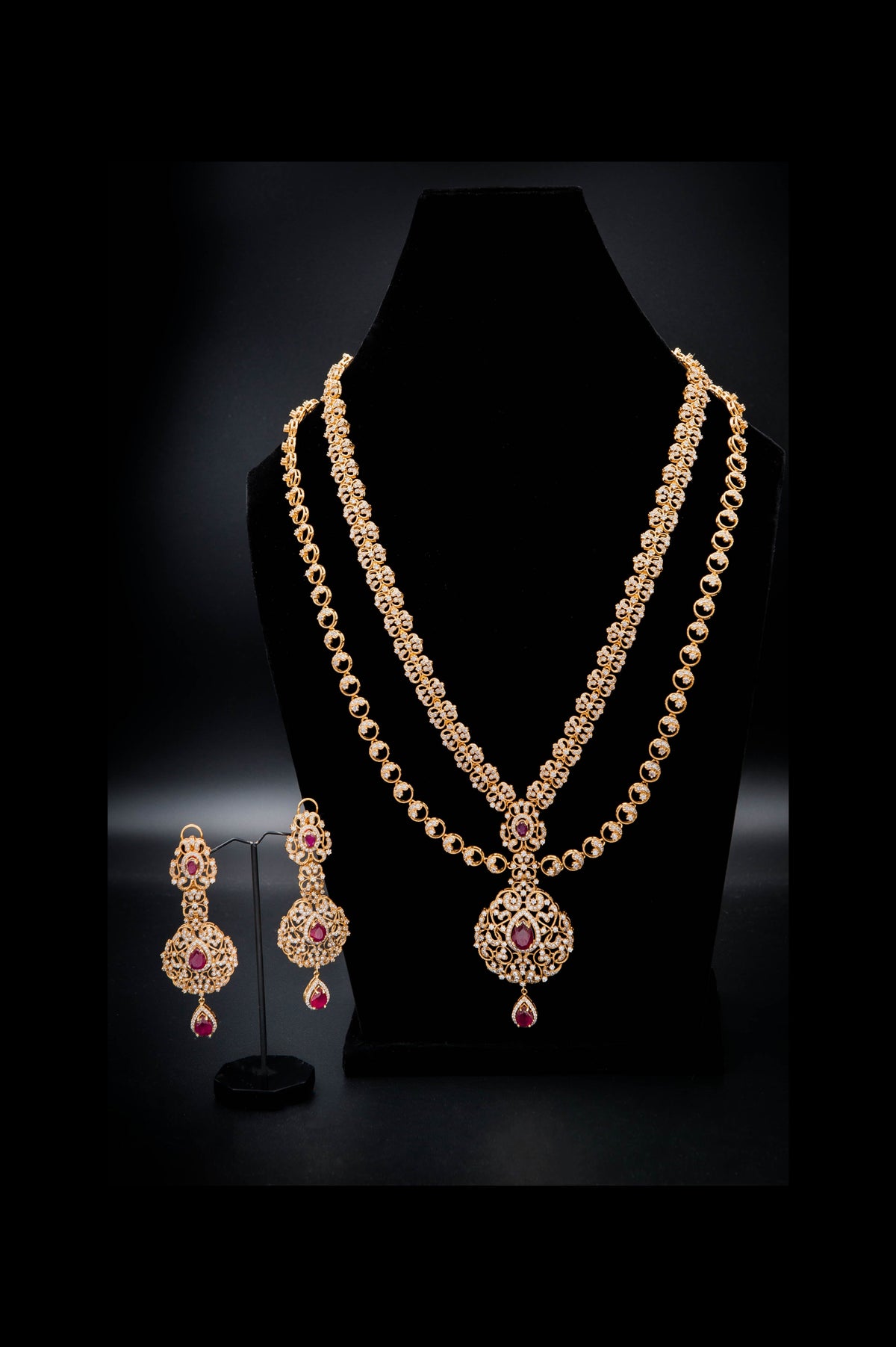 Gold necklace with pendant and matching earrings on a black stand against a dark background