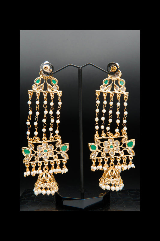 Pair of gold earrings with pearls and green stones on a black stand