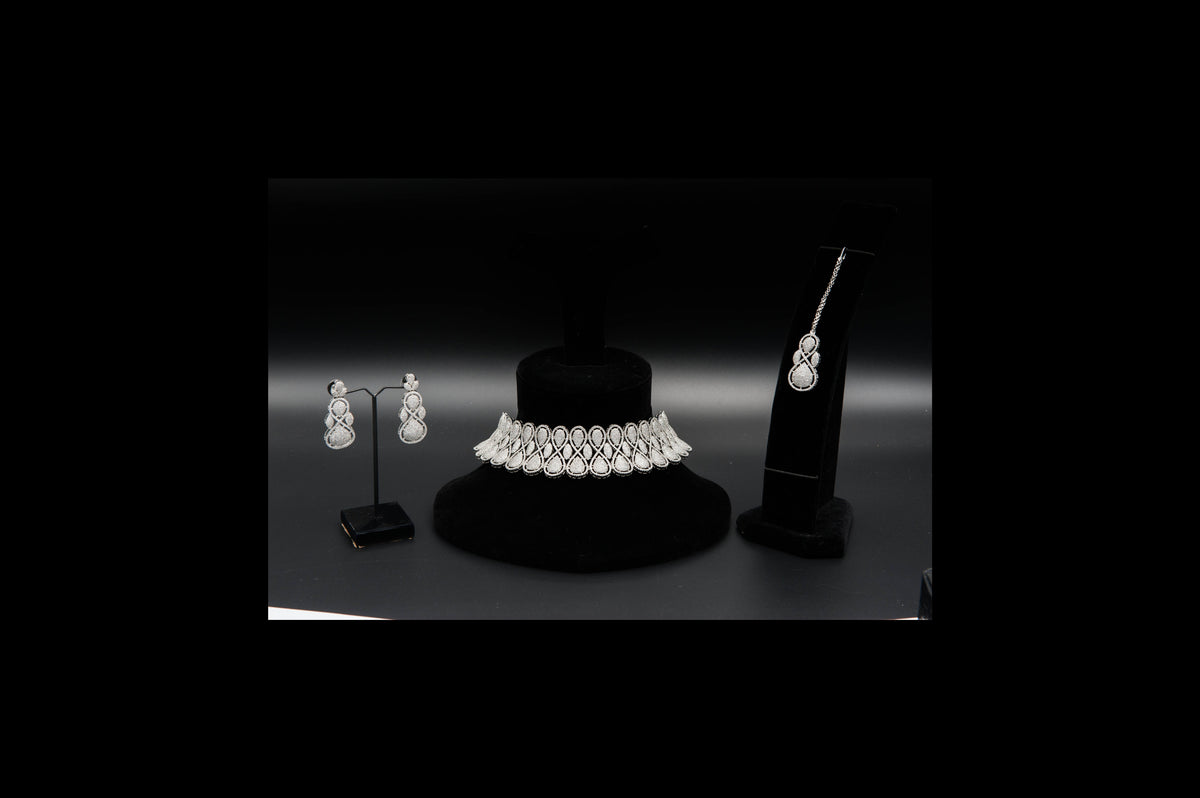 Jewelry set including a necklace and earrings on black stands against a dark background