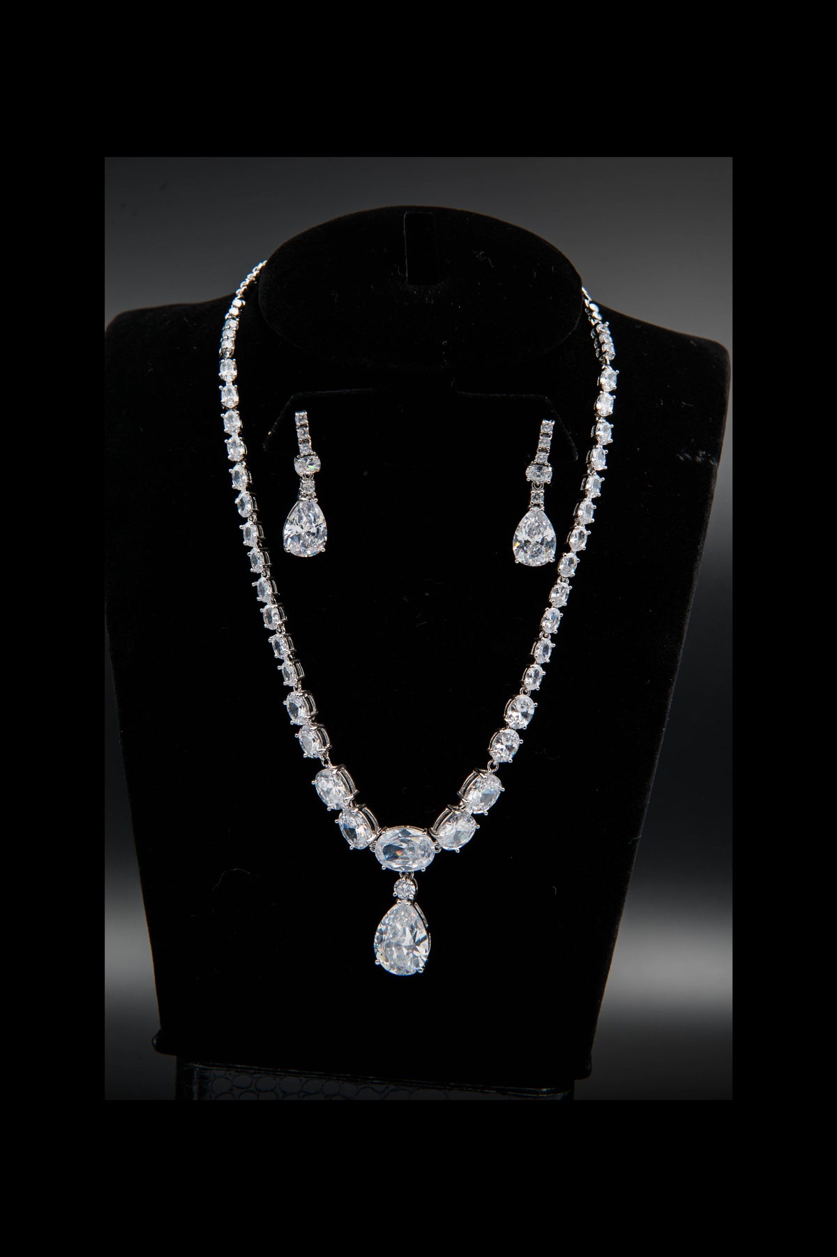 Diamond necklace and earrings set on a black mannequin bust against a dark background